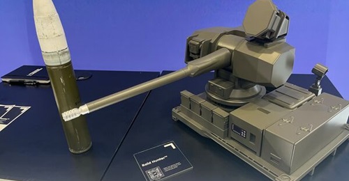 A scale-model Northrop Grumman's Raid Hunter gun-based C-UAS system alongside a model 50 mm round.