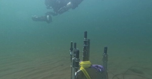 A passive acoustic detection pod sits on the seabed with a diver swimming nearby during Saab's underwater trials at a test site in Sweden. The individual system is integrated within Saab's wider Ocean Barrier network.