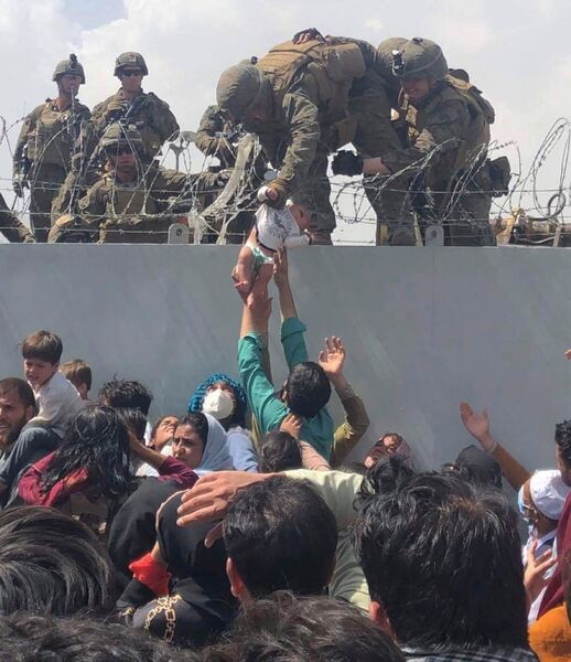 A US Marine grabs an infant over a fence of barbed wire during the evacuation at Hamid Karzai International Airport in Kabul, Afghanistan, on 19 August 2021. Dozens of people were killed a week later on 26 August, at the Abbey Gate at the airport, as they queued for permission to evacuate. (Courtesy of Omar Haidiri/AFP via Getty Images)