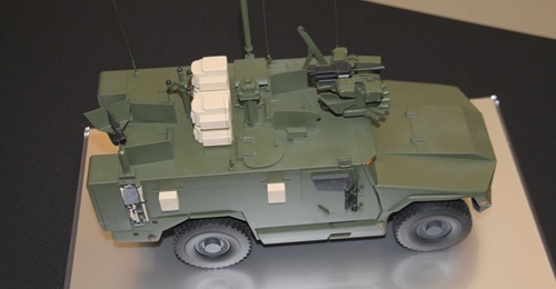 A scale model of Serval fitted with a roof-mounted remote weapon station at the front, acoustic detection system, situational awareness system, counter-improvised explosive device equipment, and pintle-mounted machine gun.