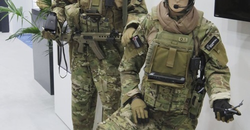 The Rheinmetall Canada Argus soldier system displayed at IDEX 19 with the baseline Saab Linux display (left) and the chest-mounted Windows tablet for commanders (right). The antenna for the MPU5 is visible over the left-hand model's left shoulder.