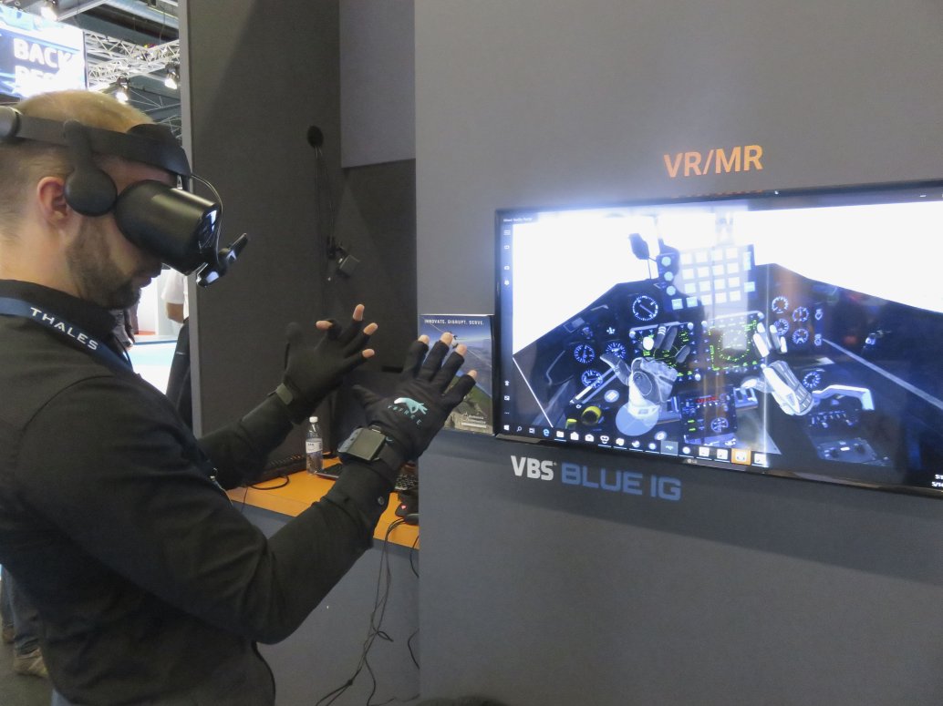 The VRfree system demonstrated at ITEC 2019. The tracking device is mounted on the front of the head-mounted display (HMD). The screen shows the view of the virtual environment shown in the HMD. The hands can be seen in front of the cockpit controls. (Giles Ebbutt)