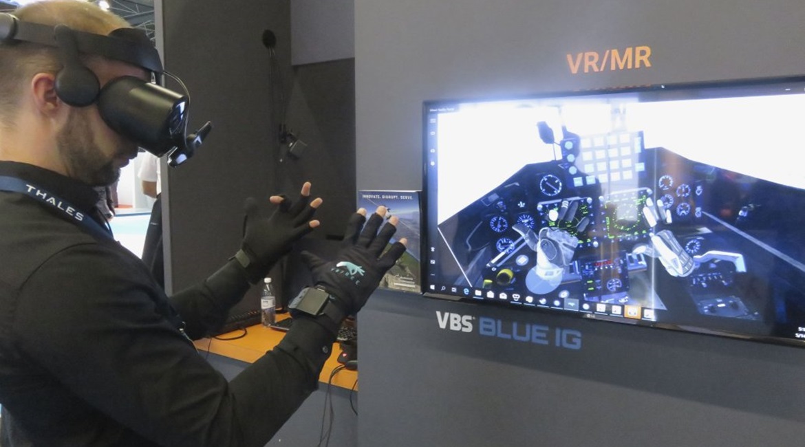 The VRfree system demonstrated at ITEC 2019. The tracking device is mounted on the front of the head-mounted display (HMD). The screen shows the view of the virtual environment shown in the HMD. The hands can be seen in front of the cockpit controls.