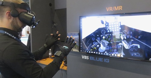 The VRfree system demonstrated at ITEC 2019. The tracking device is mounted on the front of the head-mounted display (HMD). The screen shows the view of the virtual environment shown in the HMD. The hands can be seen in front of the cockpit controls.