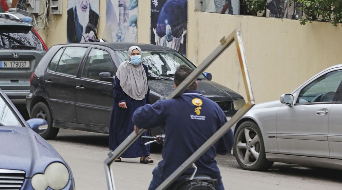 A woman, wearing a face mask amid coronavirus fears, crosses a street with a portrait of Iran's former Supreme Leader Ayatollah Ruhollah Khomeini hanging on the wall in Beirut's southern suburb of Chiyah on 14 March 2020.