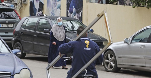 A woman, wearing a face mask amid coronavirus fears, crosses a street with a portrait of Iran's former Supreme Leader Ayatollah Ruhollah Khomeini hanging on the wall in Beirut's southern suburb of Chiyah on 14 March 2020.