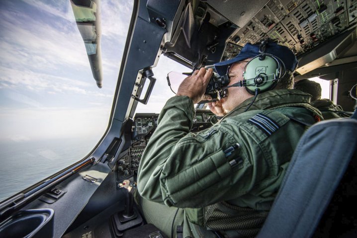 An RAF A400M crew member using binoculars to scan the English Channel for migrant boats. (Crown copyright)