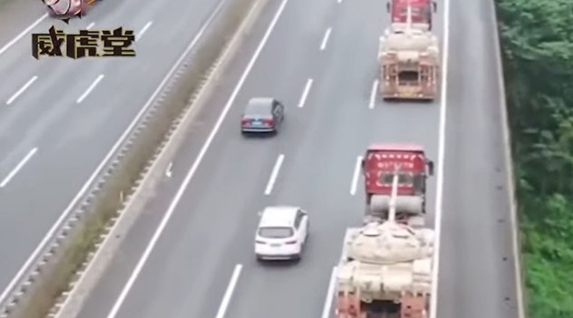 A screenshot from CCTV 7 footage released on 17 November showing two modified civilian flatbed trucks on a Chinese road transporting PLAGF Type 59D MBTs.