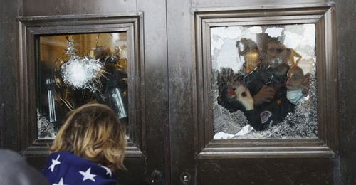 A photograph depicting pro-Trump protesters attempting to enter the Capitol Building, glass on the doors of which has been damaged.