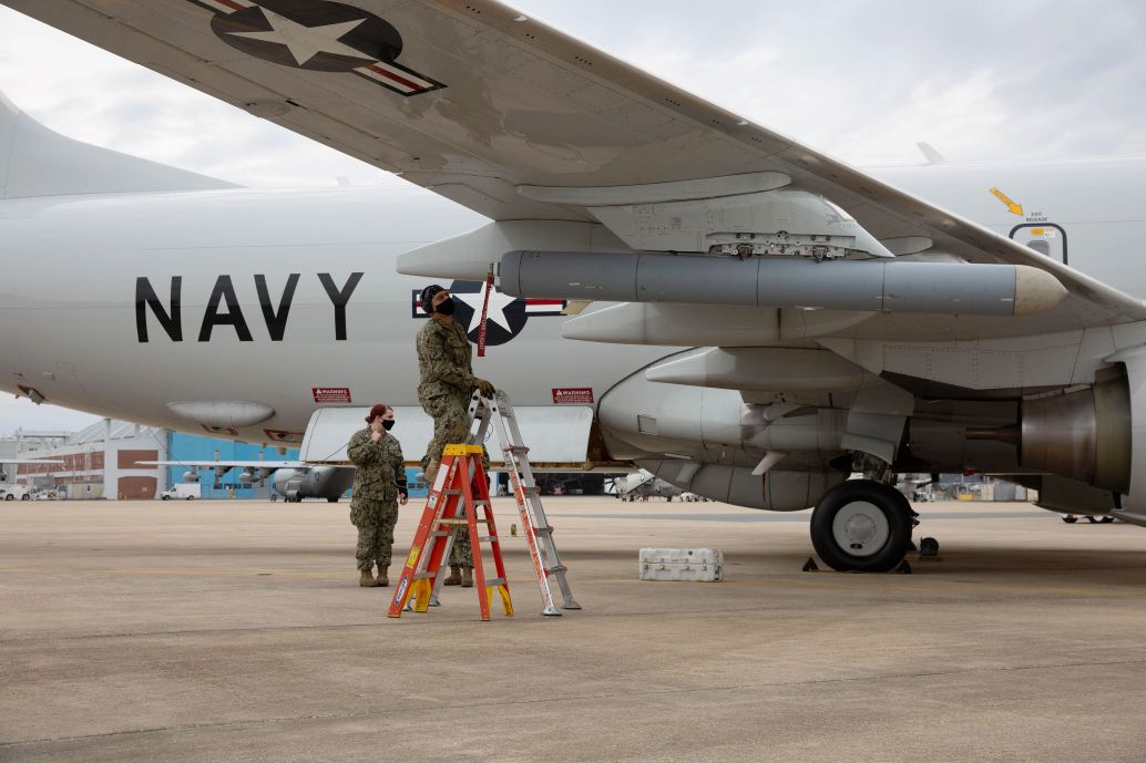 A member of the Air Test and Evaluation Squadron (VX) 20 puts a pod-mounted radio frequency countermeasure system on a P-8A Poseidon. (US Navy)